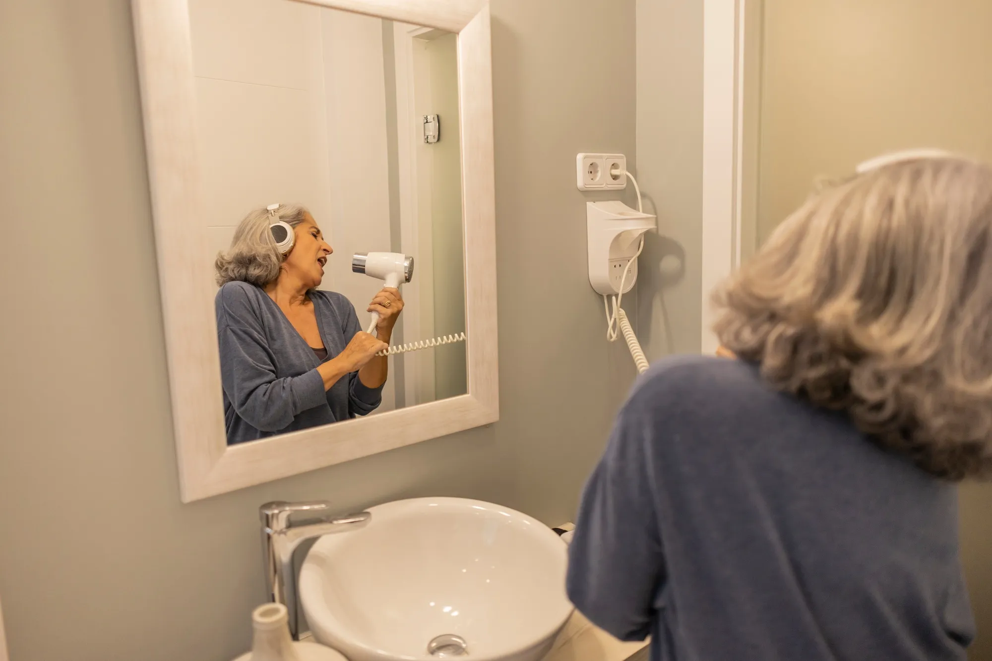 Portrait of senior woman wearing headphones and bathrobe indoors at home.