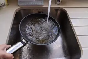Frying pan with non-stick surface and hot oil under water tap flow in sink. Care kitchenware concept
