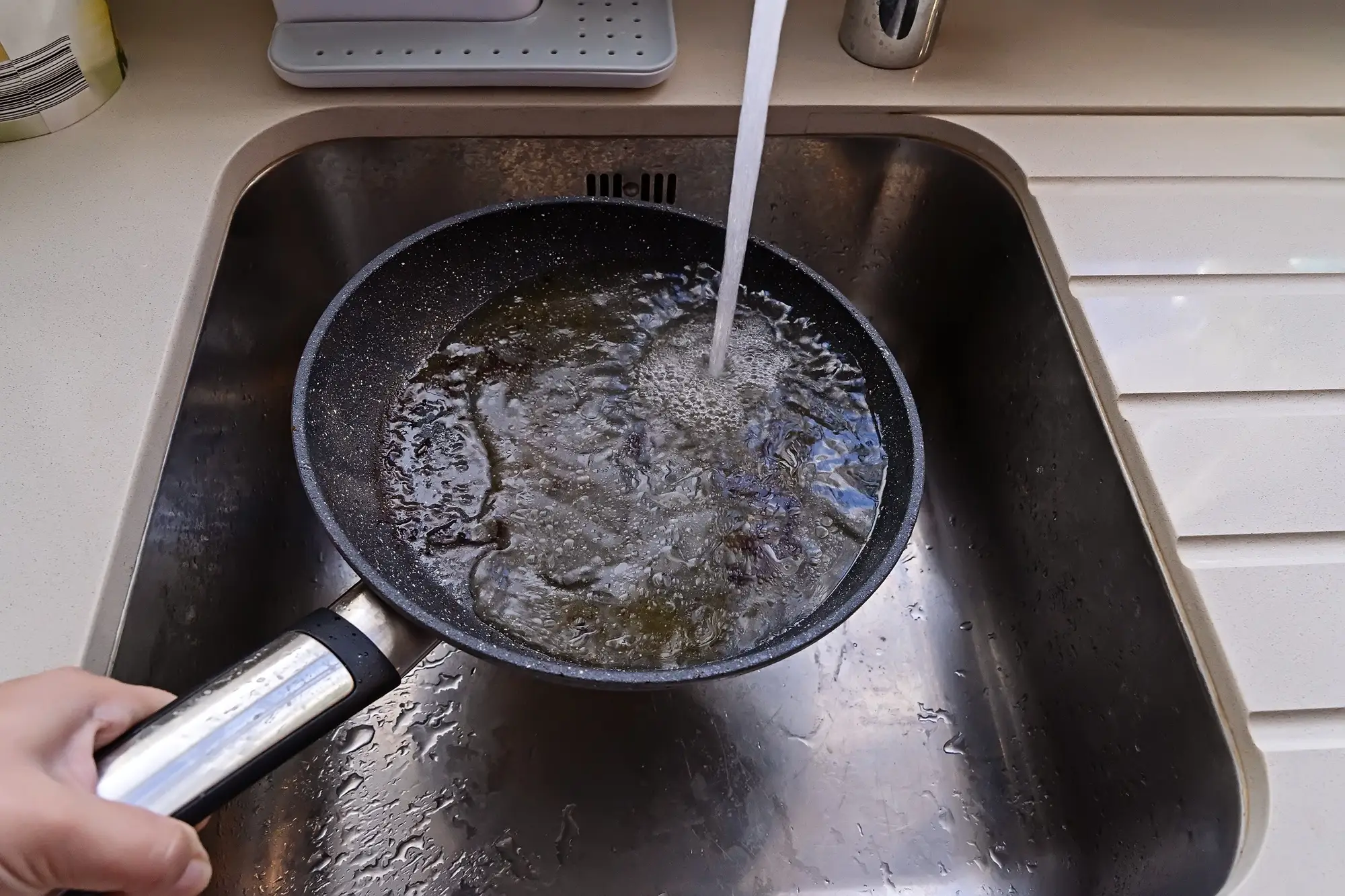 Frying pan with non-stick surface and hot oil under water tap flow in sink. Care kitchenware concept