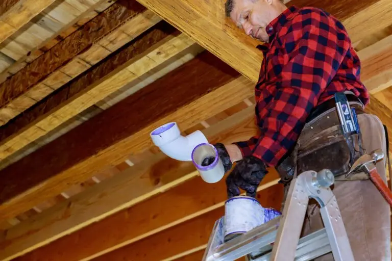 Plombier en train d’installer un tuyau en PVC sous une charpente en bois